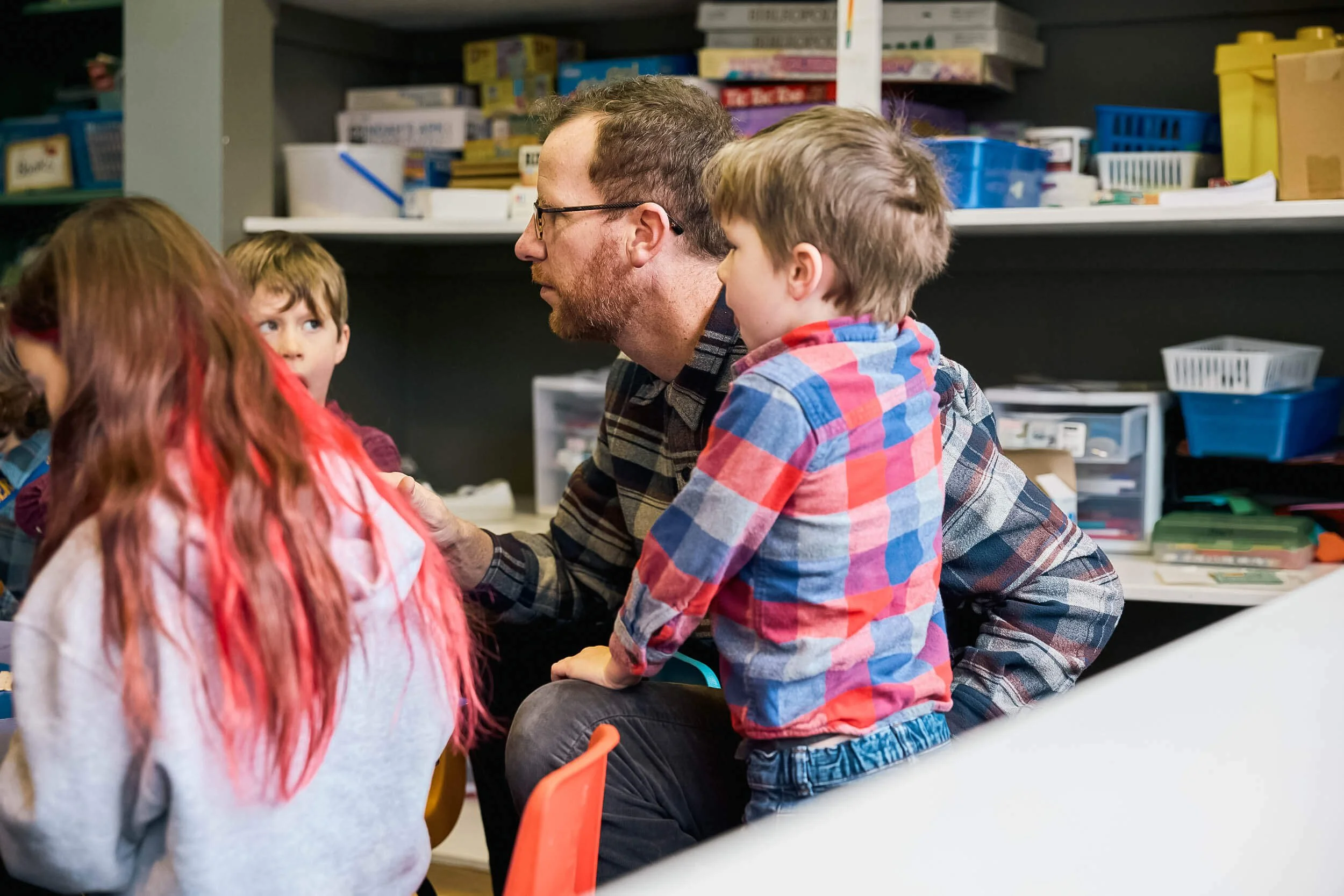 An adult and young elementary aged child sit side by side, looking on as the group works on an activity together during Sunday school at Crown Hill Church.
