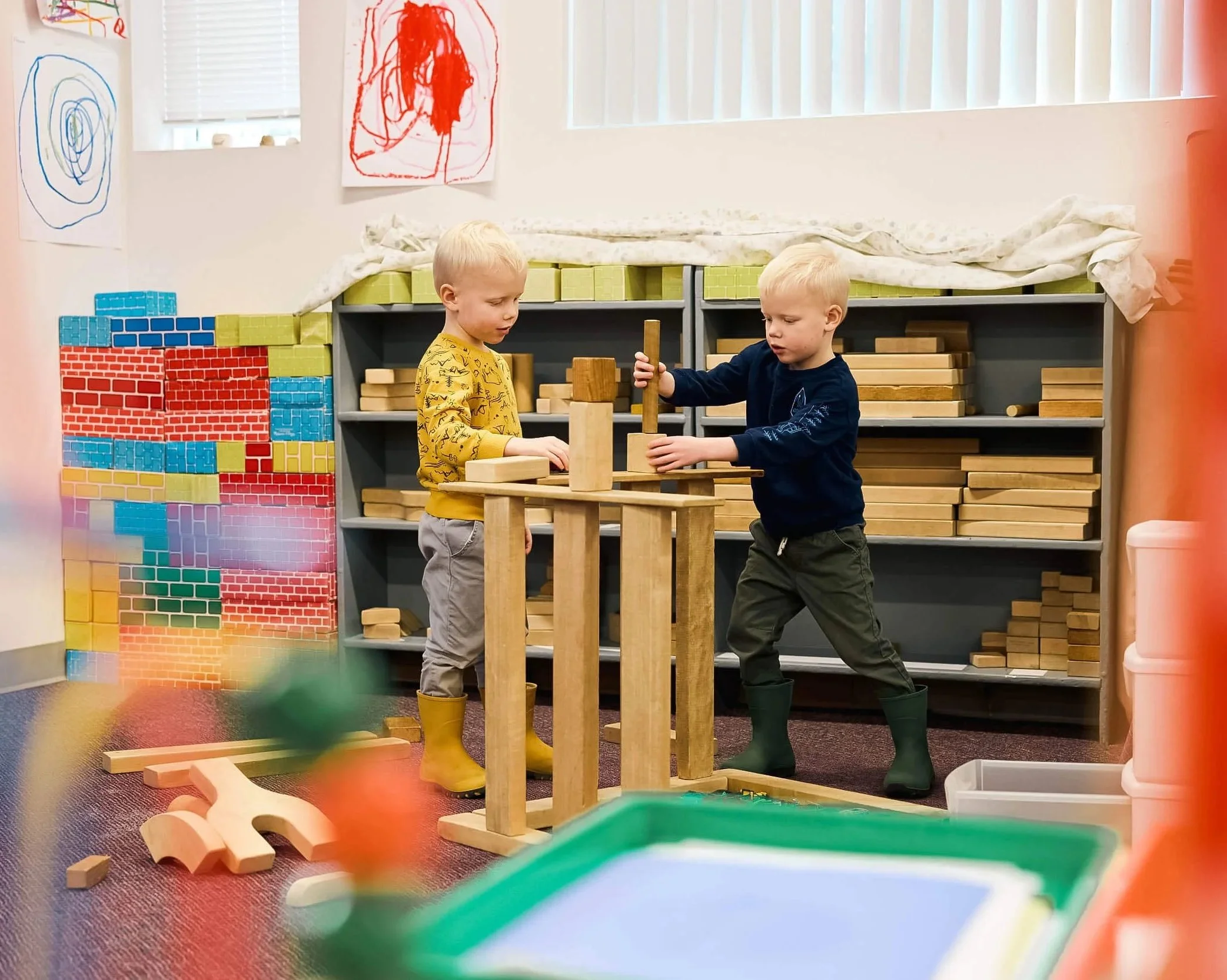 Two boys work together stacking large wooden blocks to build a tall structure at PATH Preschool.