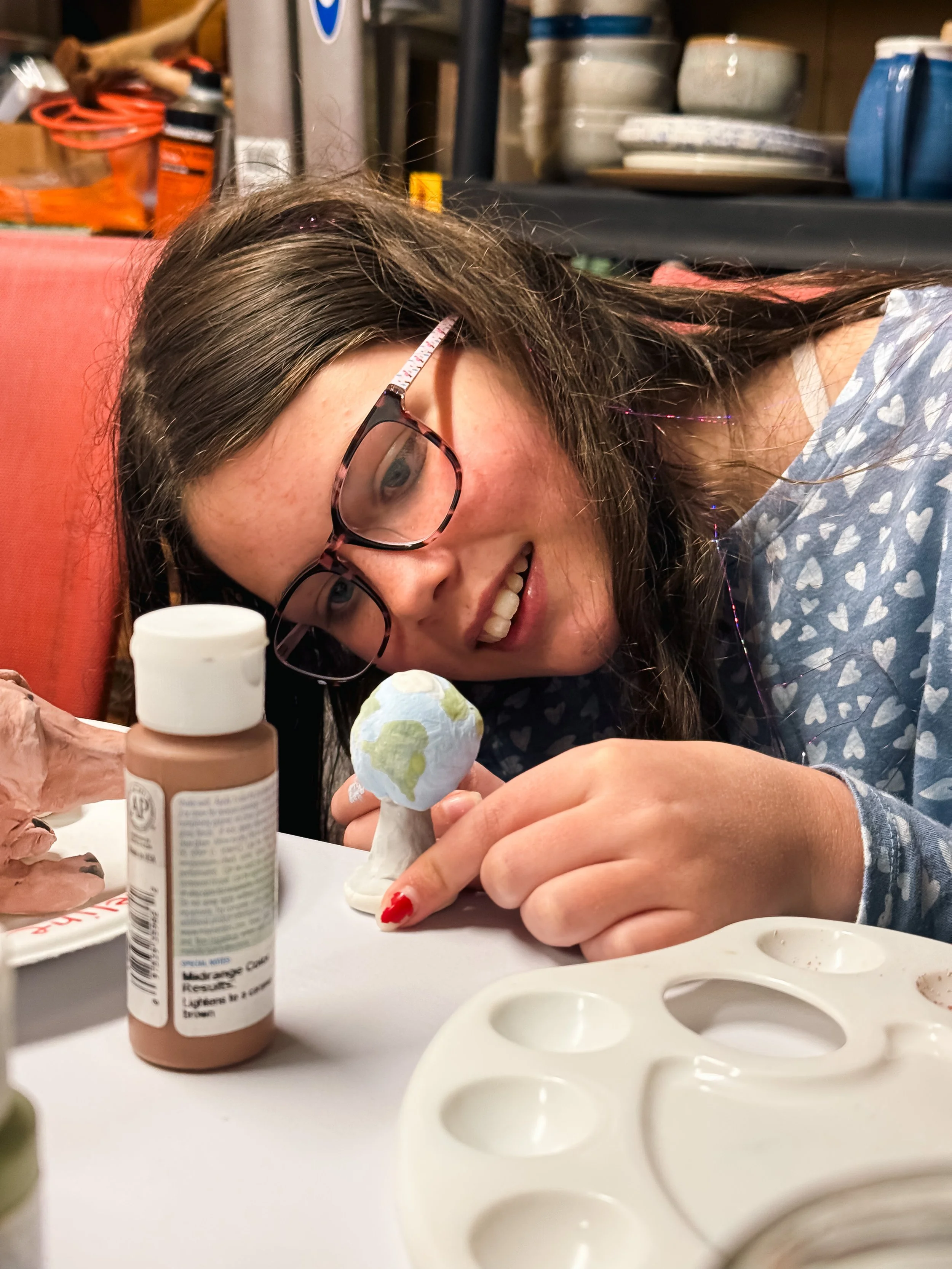 A tween girl carefully paints a clay earth during a Curious Minds Club creative project event at Crown Hill Church in Seattle's Crown Hill neighborhood.