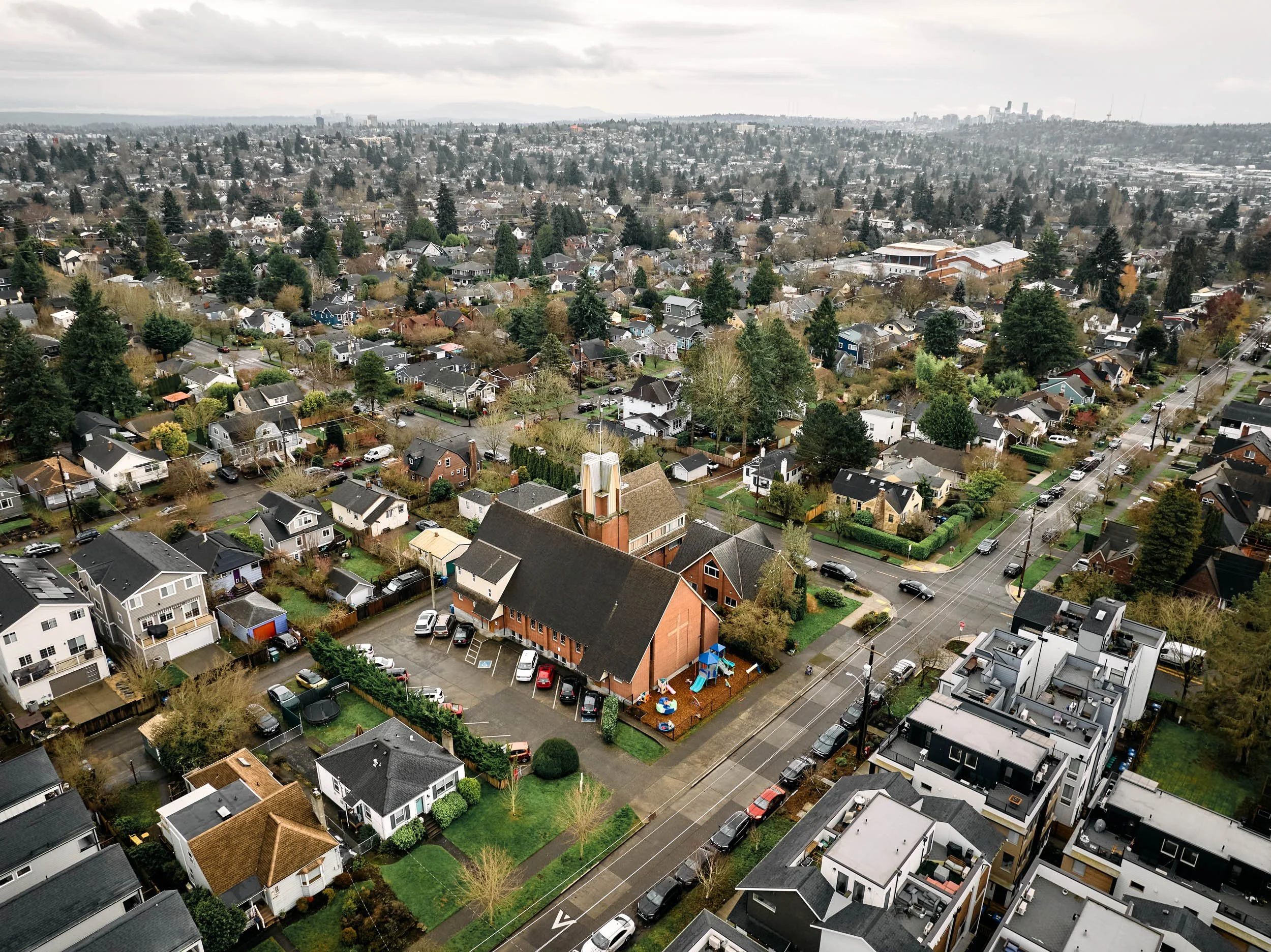 An aerial drone image of Crown Hill Church nestled within the Crown Hill neighborhood of Seattle, with the Seattle city skyline visible in the distance.