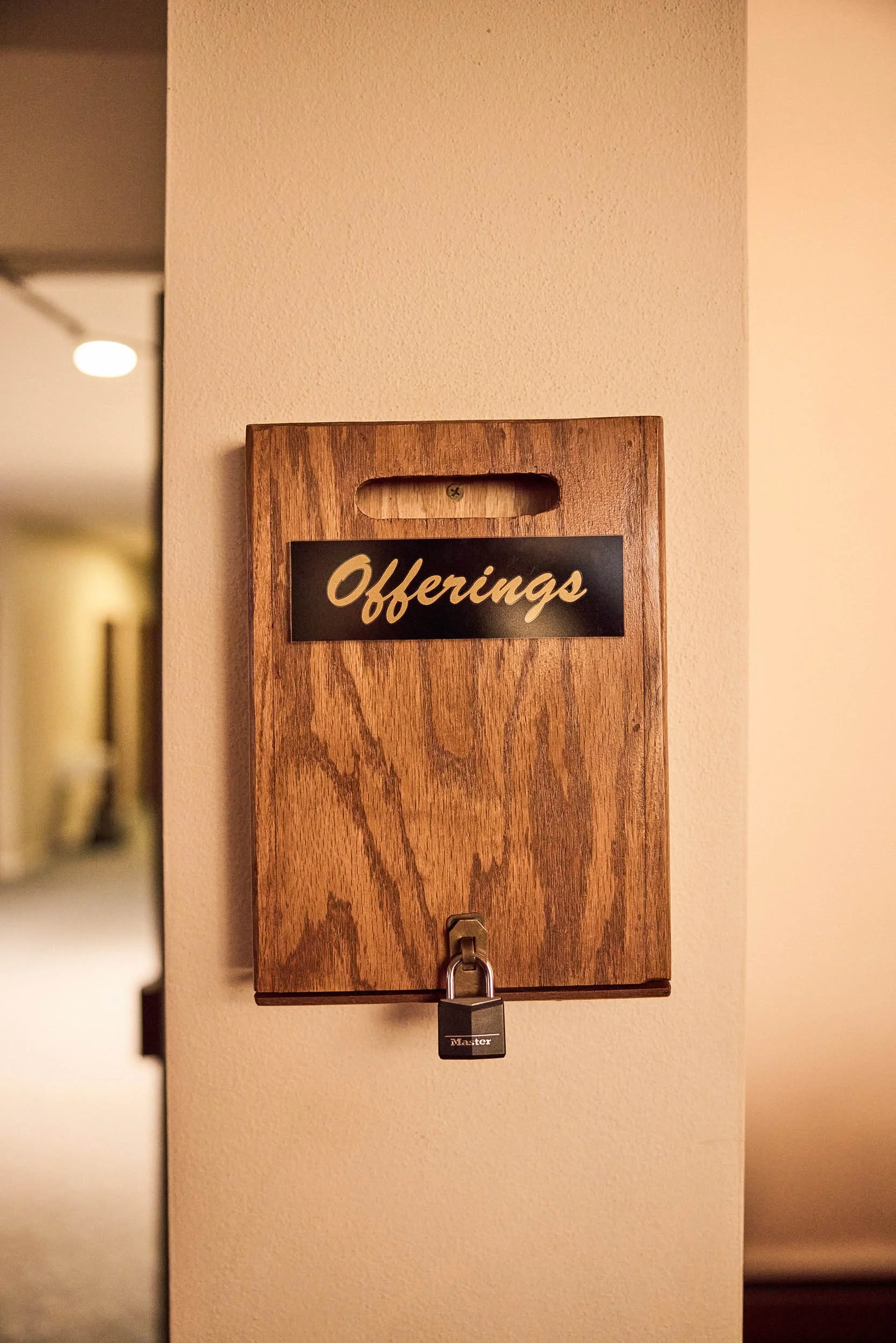 A wood offering box mounted to the wall at the back of the sanctuary for in-person giving at Crown Hill Church.