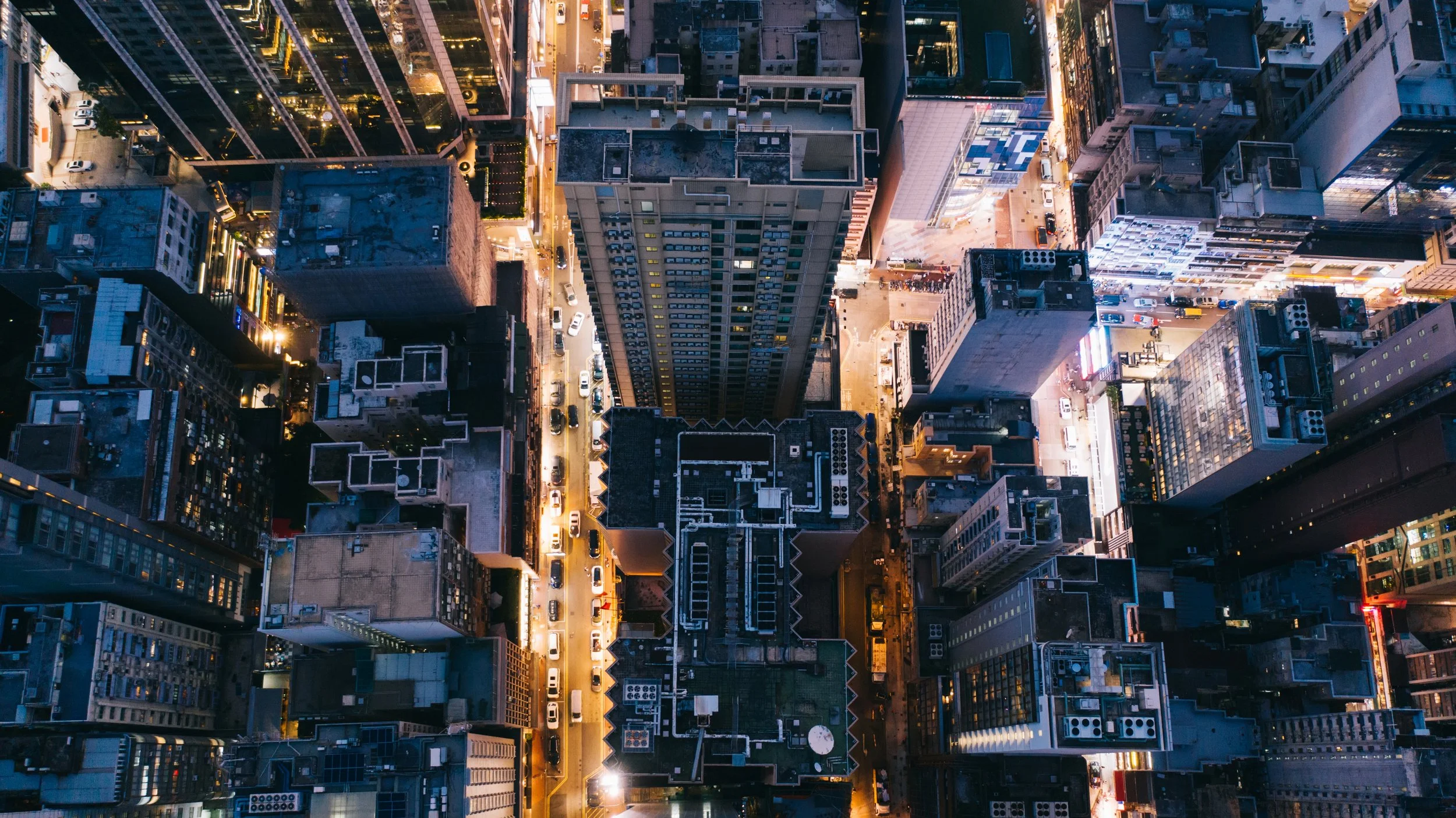 An aerial night-time view of a city with tall buildings and illuminated streets.