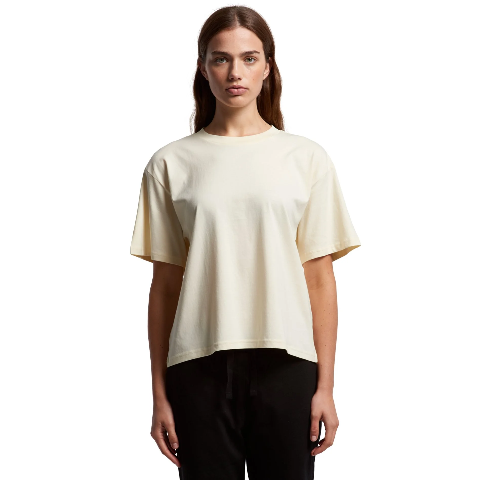 A woman with long red hair wearing a loose cream-colored T-shirt and black pants, standing against a white background.