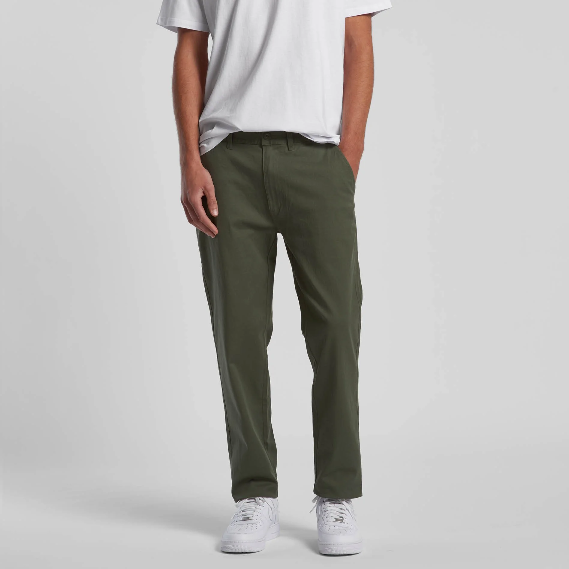 Person wearing a white t-shirt, green pants, and white sneakers, standing against a gray background.
