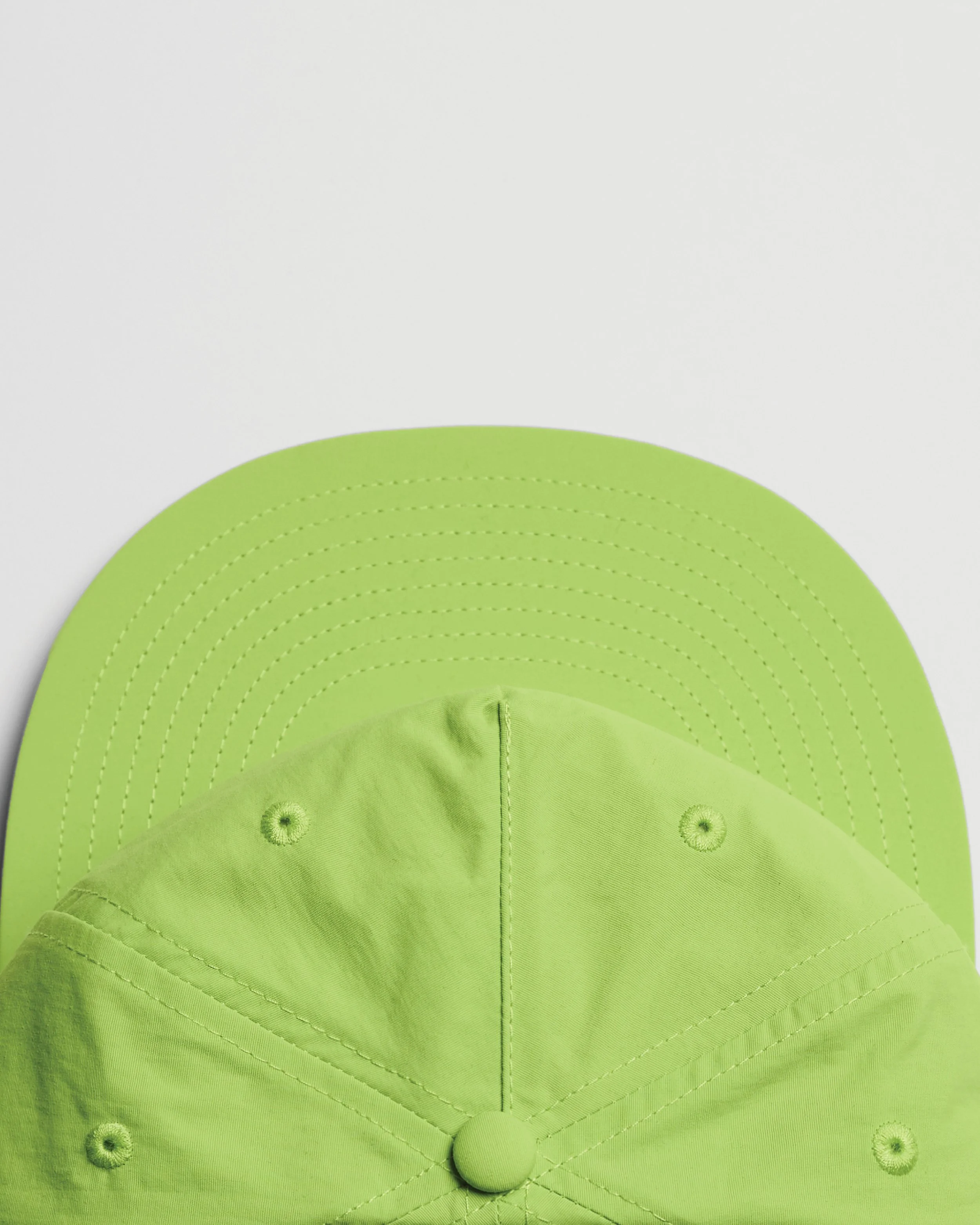 Close-up view of the top of a lime green baseball cap, showing stitched concentric semicircles and buttons around the brim, with a knot at the front.
