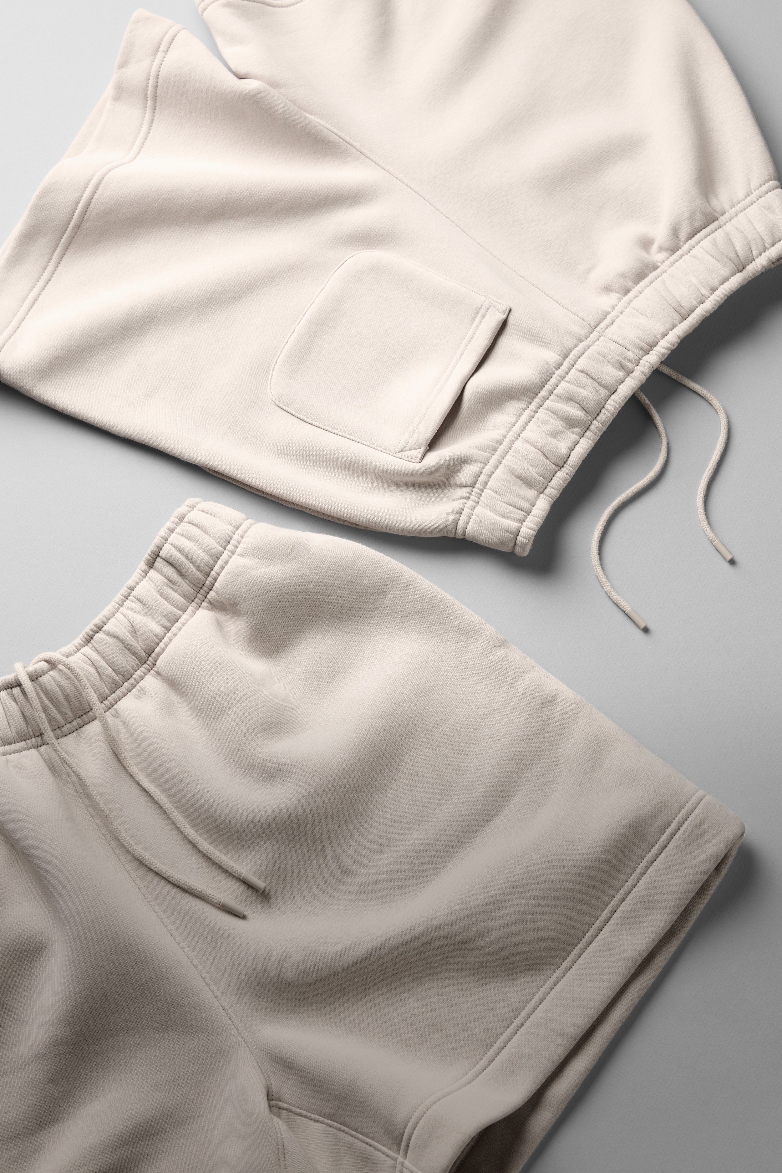 Close-up of a beige hoodie with a front pocket and drawstrings on the hood, placed on a light grey surface.