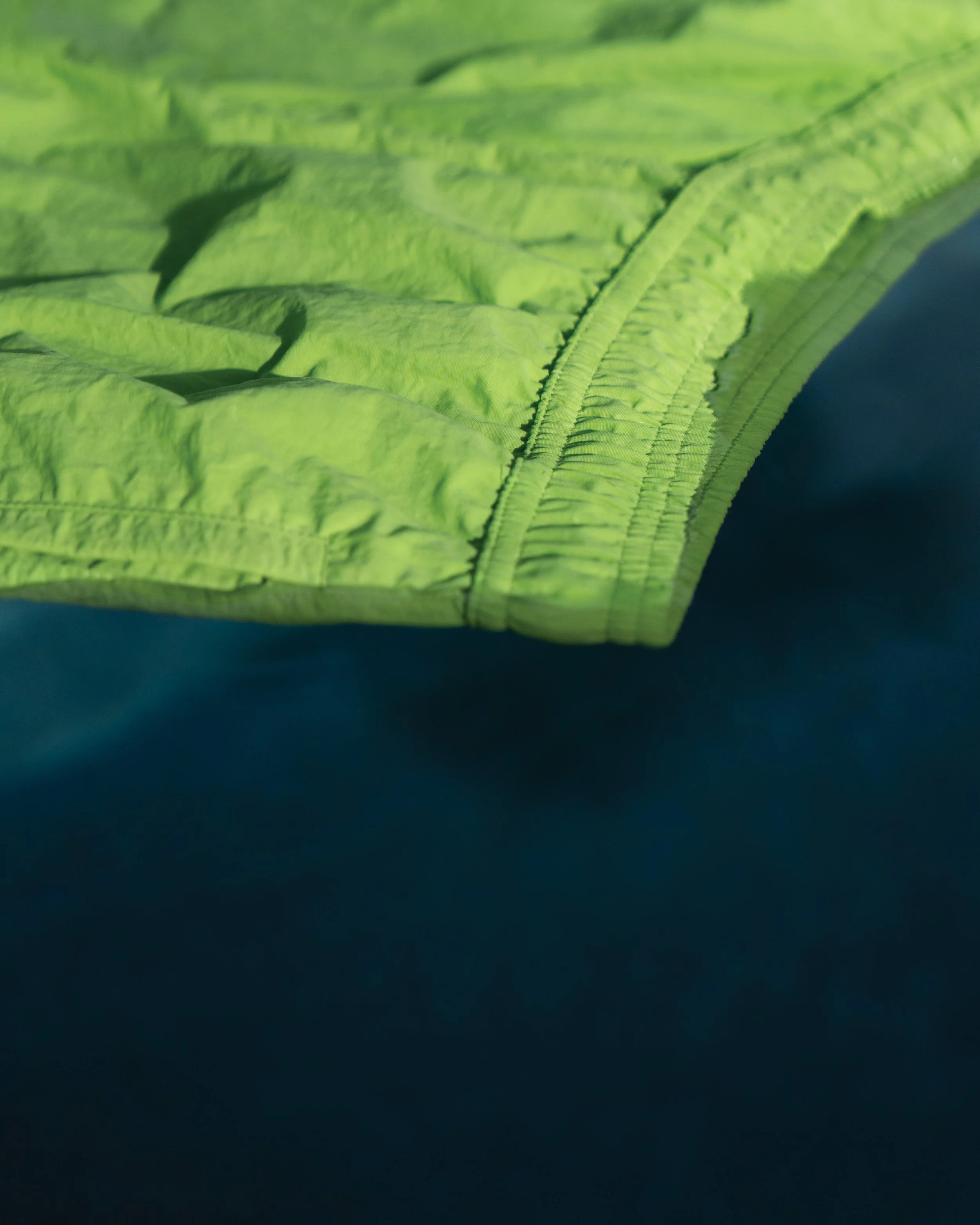 Close-up of a green fabric with a zipper, possibly part of a jacket or outdoor gear, against a dark background.