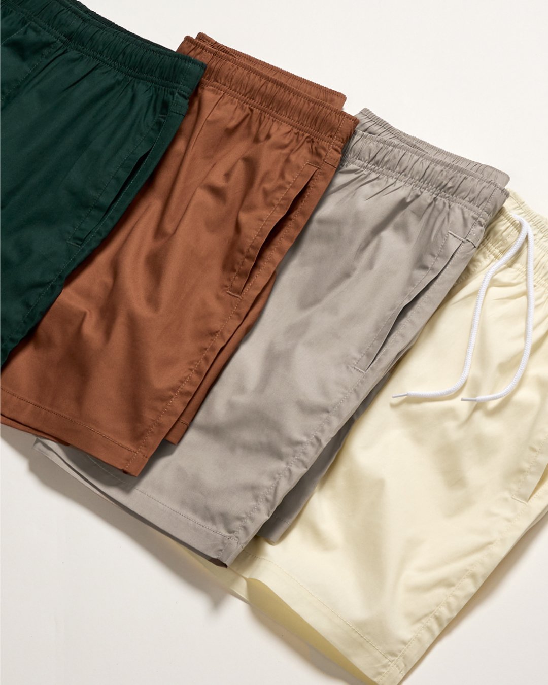 Four pairs of shorts in green, brown, gray, and yellow, laid out on a white surface.