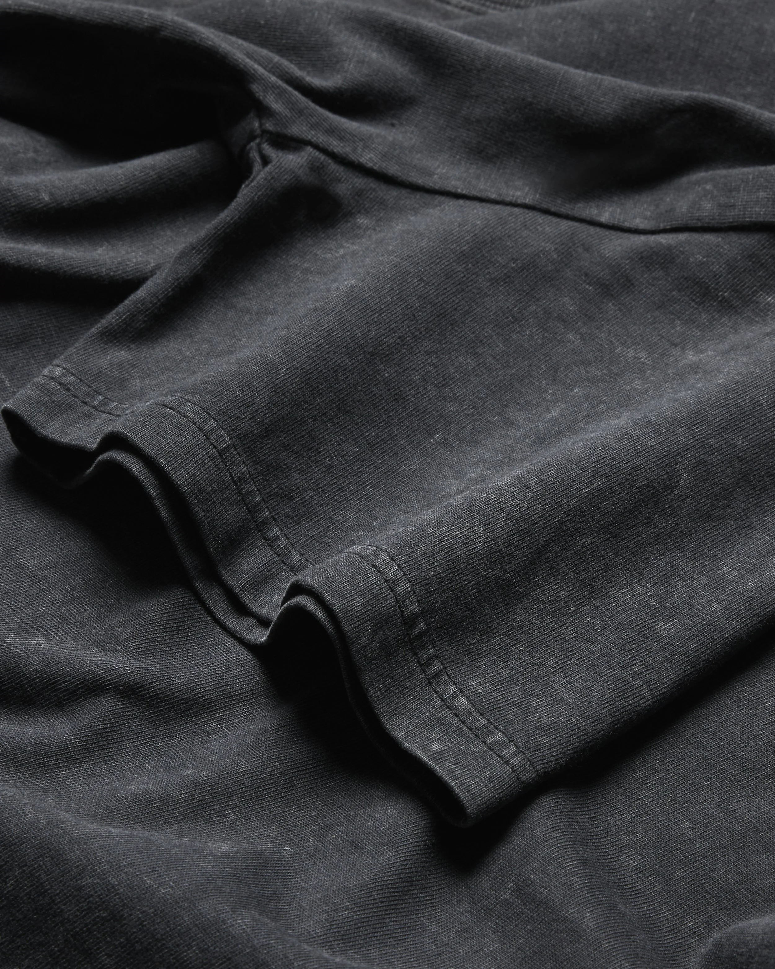Close-up of folded black or dark gray fabric, possibly clothing or a textile material, with visible stitching.