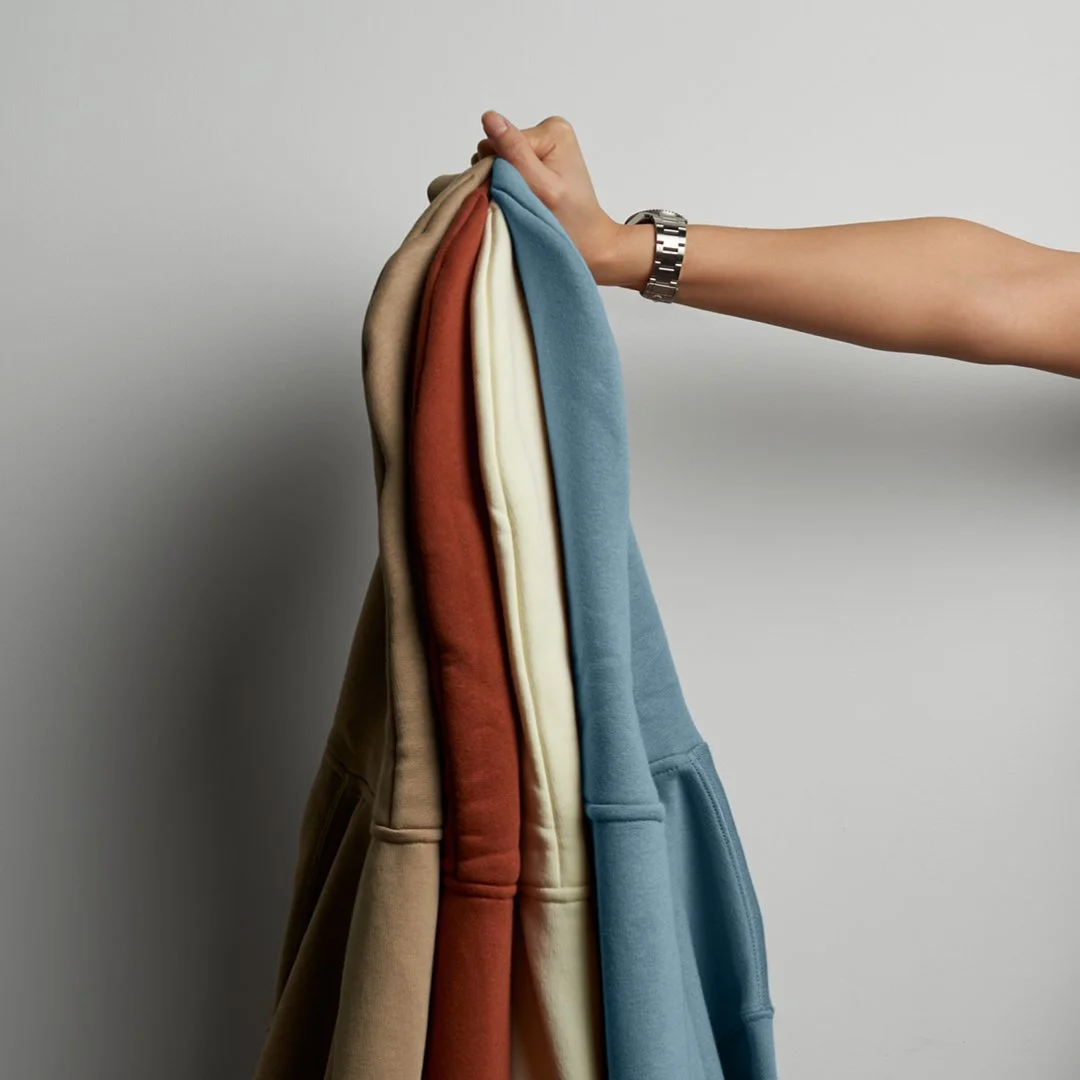 A hand holding several sweatshirts in various colors against a plain background.