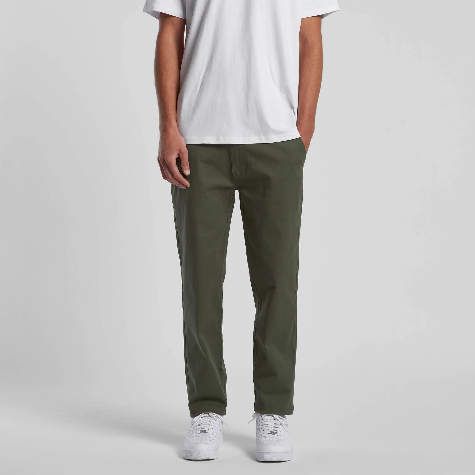 A person is wearing a white t-shirt, dark green pants, and white sneakers, standing against a plain gray background.