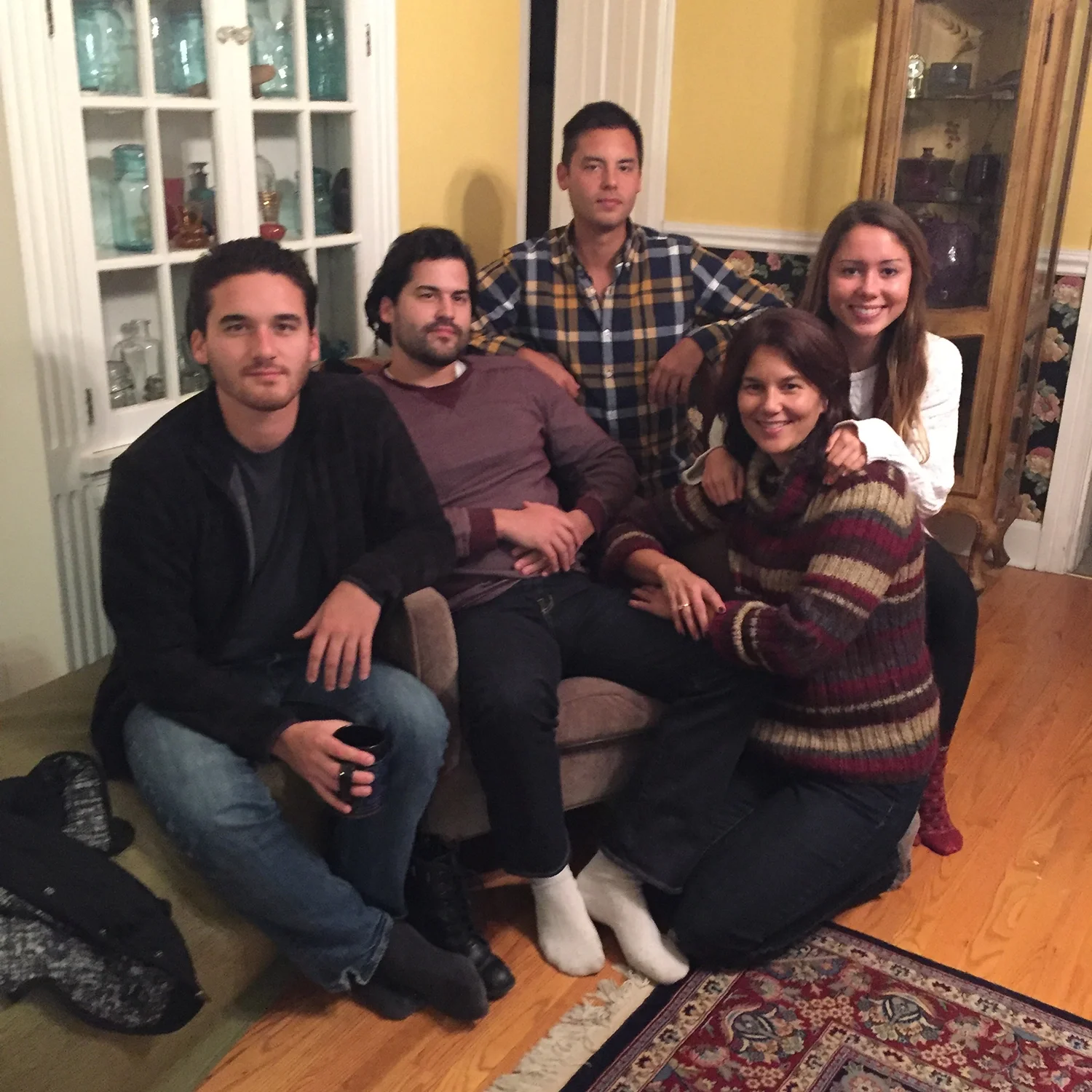 Group of five people sitting together in a living room, smiling and posing for a photo.