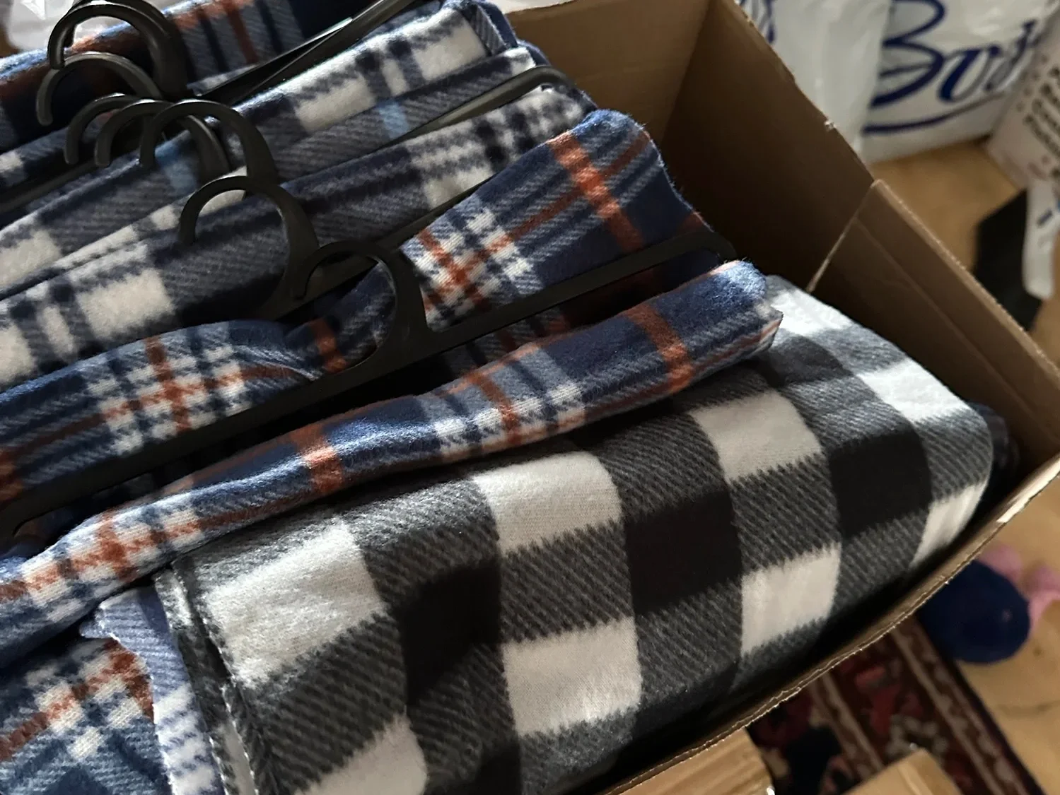 Folded plaid blankets stacked in a box, prepared for donation and distribution.