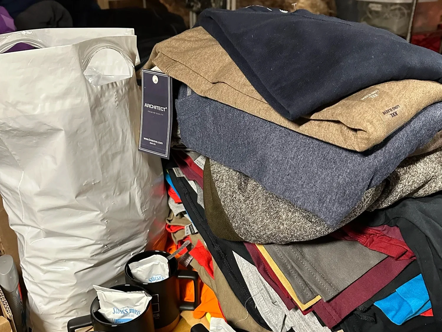 Stack of folded clothing and winter apparel next to a donation bag and supplies.
