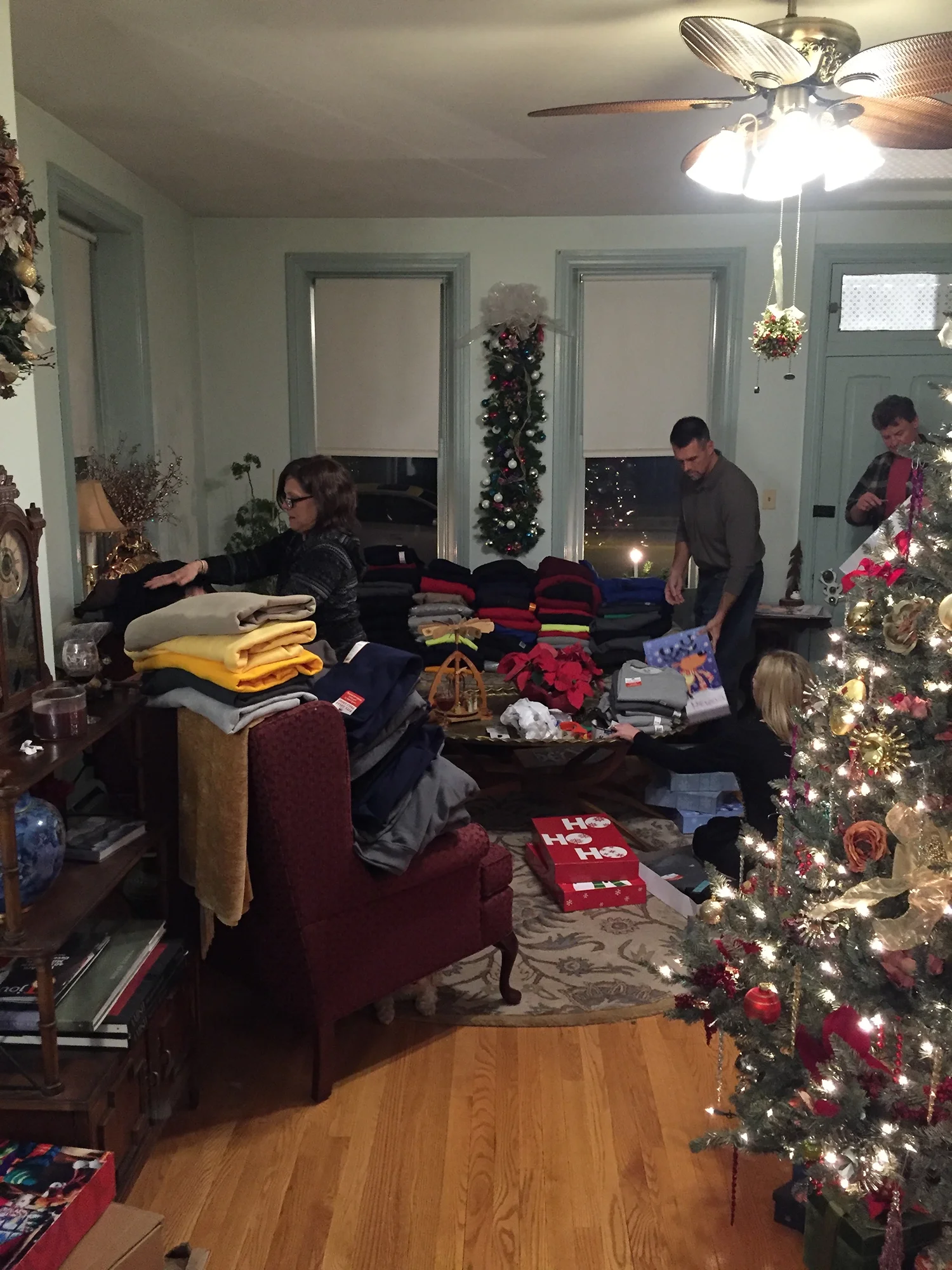 Volunteers gather in a living room, organizing folded blankets and gifts around a decorated Christmas tree.