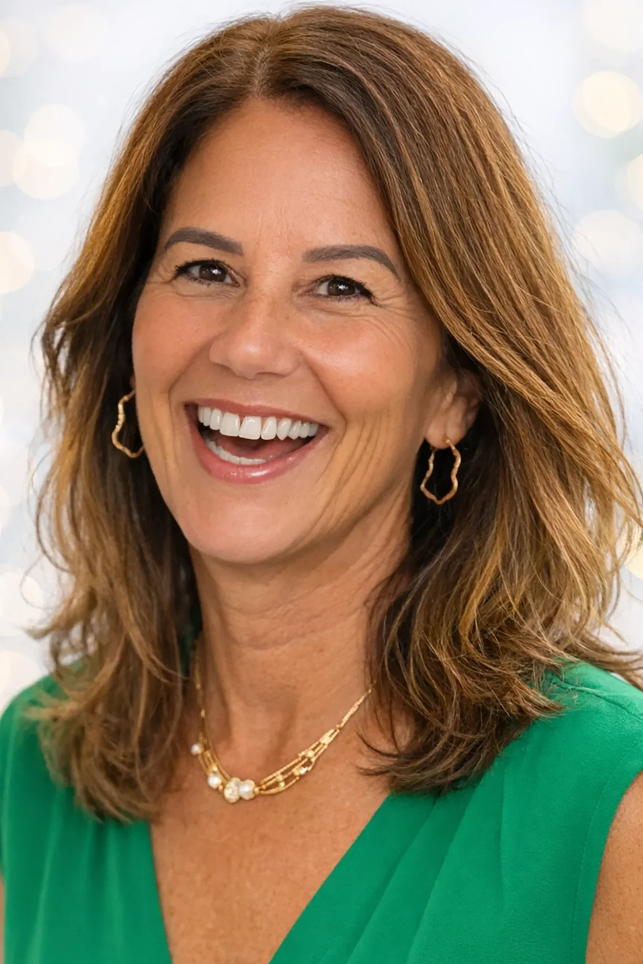 Smiling woman with auburn hair wearing gold jewelry and a green top.