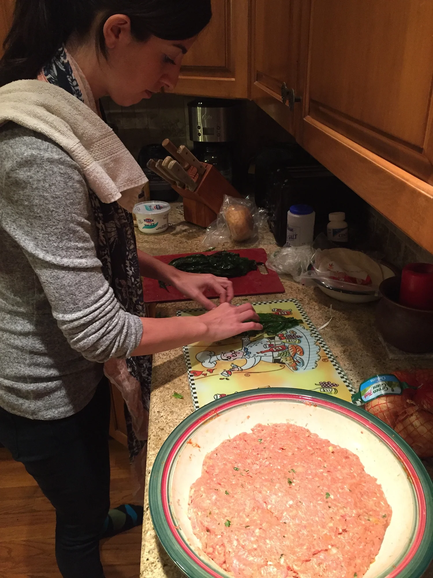 Woman preparing food in a kitchen, chopping greens on a cutting board with a bowl of seasoned ground meat nearby.