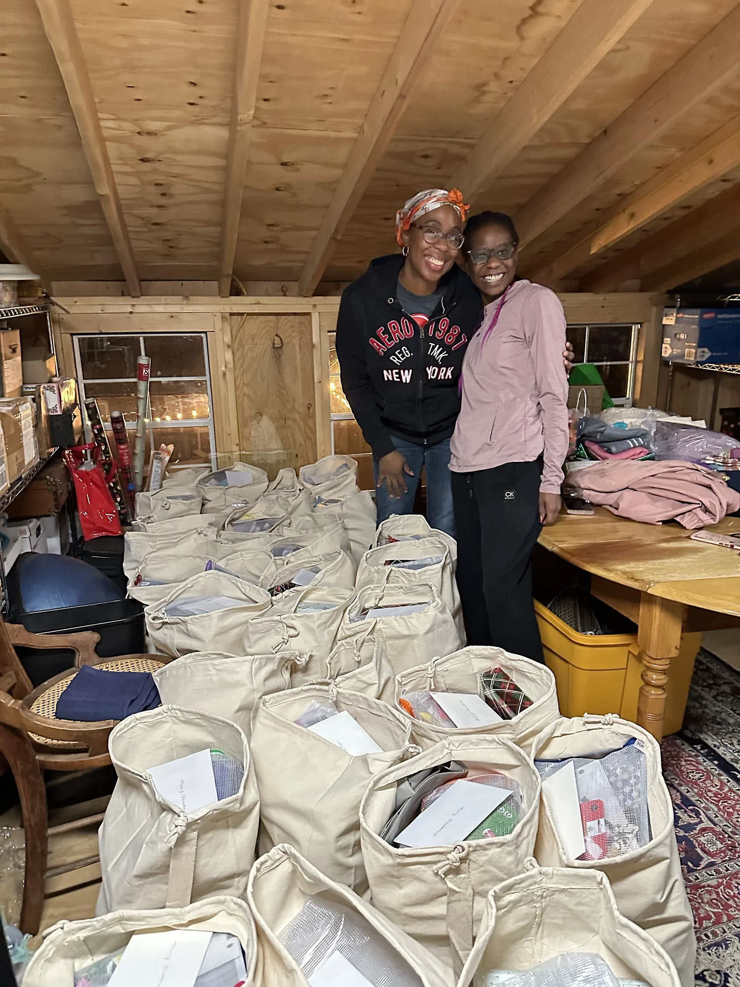 Two volunteers smiling and standing among filled donation bags prepared for community distribution.