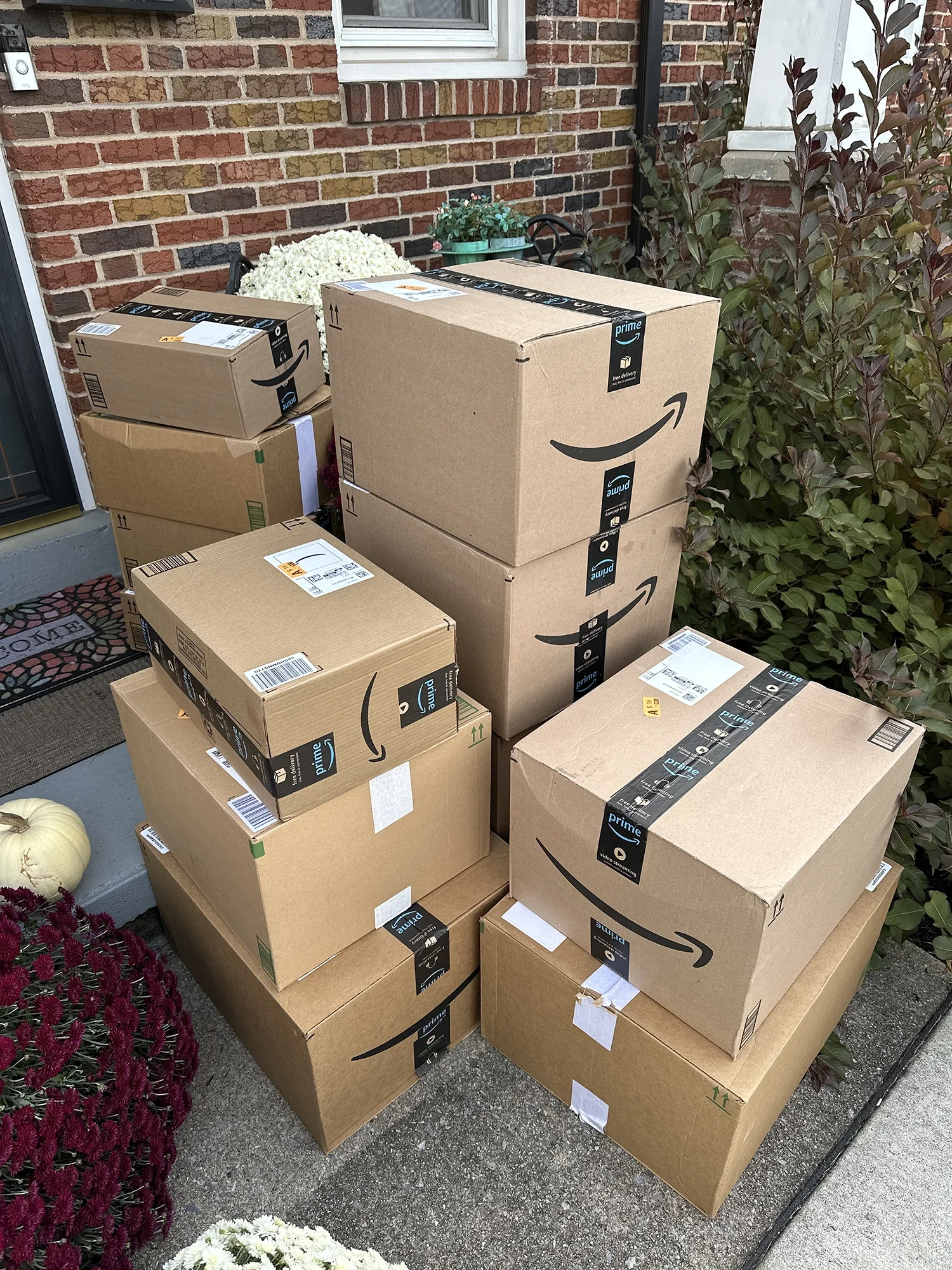 Stack of Amazon delivery boxes on a front porch, containing donated items for care packages.