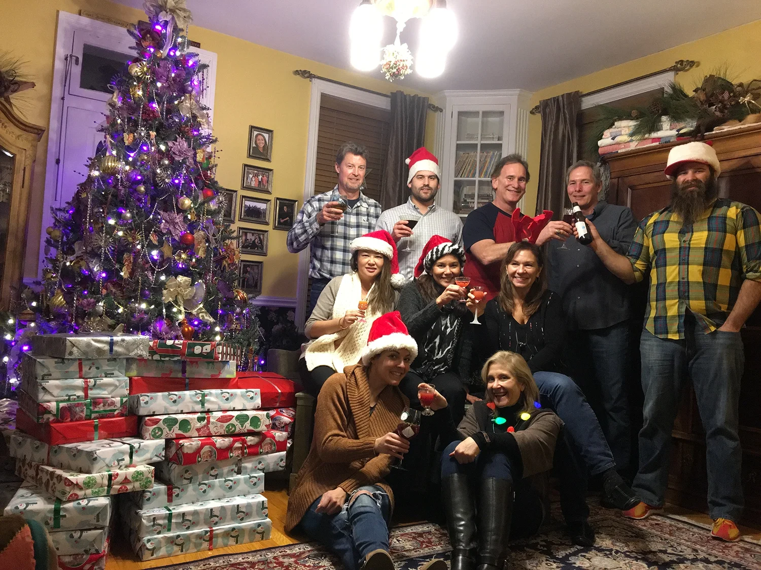 Group of volunteers gathered around a Christmas tree and wrapped gifts, celebrating during a holiday donation effort.