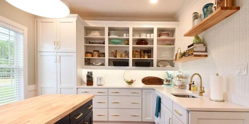Kitchen with white cabinets, open shelves with dishes, a window with blinds, a kitchen island, and a gold faucet.