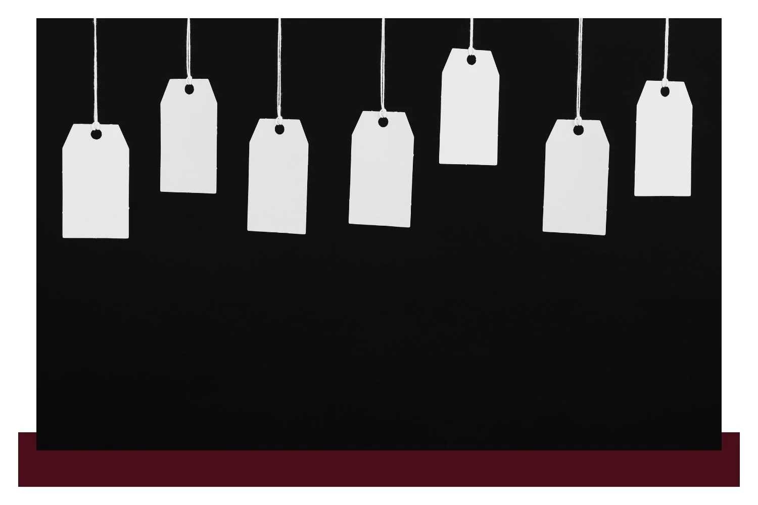 Several blank white price tags hang from thin strings against a dark black background, with five tags visible along the top and one partially cut off at the far left.