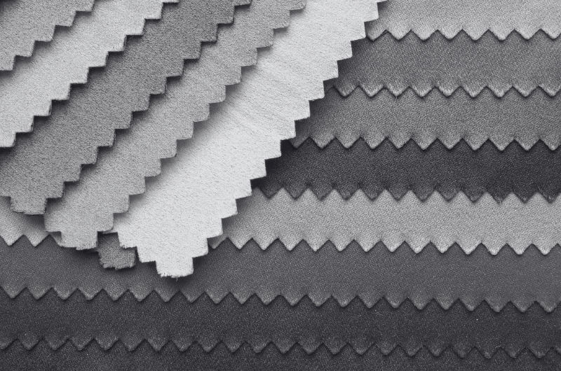 Stack of gray and dark gray fabric swatches with zigzag edges arranged in rows, showing textured woven surfaces and layered pattern.