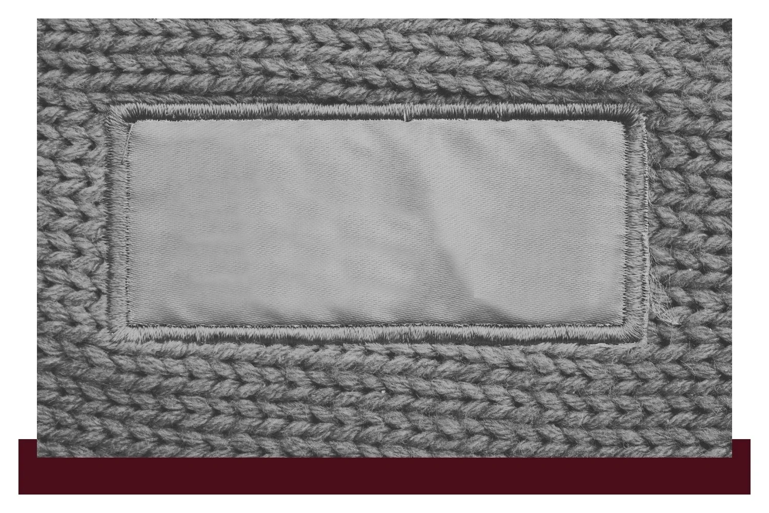 Gray textured fabric background with a rectangular light-gray stitched patch bordered by darker thread, centered in the image.