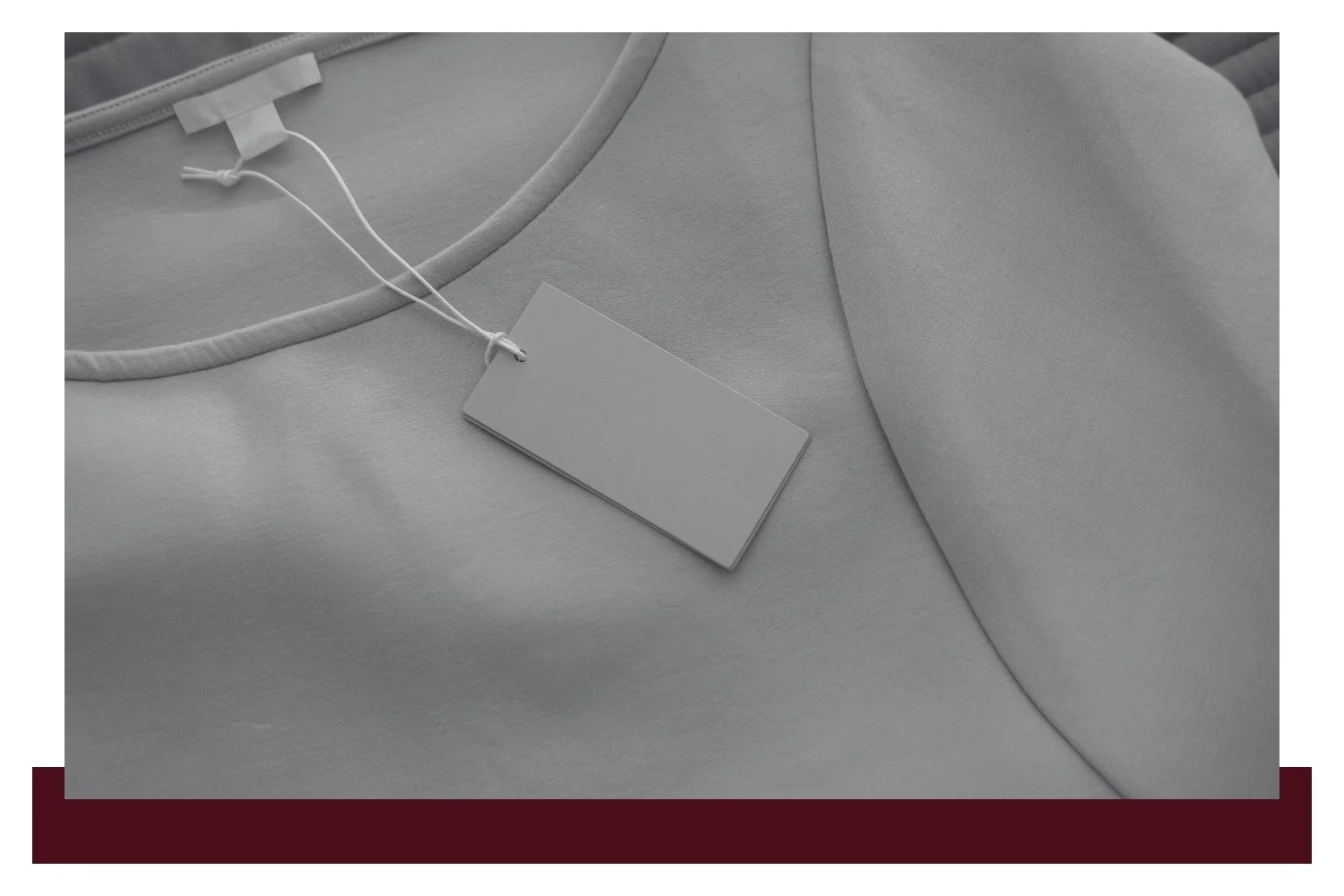 Close-up of a light gray garment with a white drawstring at the neckline and a rectangular fabric tag hanging from the string.