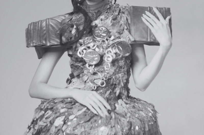 A person wearing a dramatic, textured outfit with shoulder pads resembling books and a chest piece adorned with circular embellishments.
