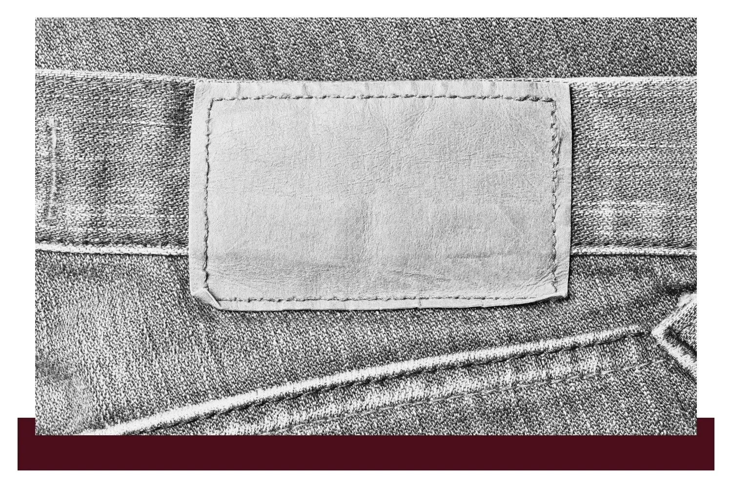 A rectangular blank fabric label with stitched edges, centered on a textured gray surface with horizontal seams.