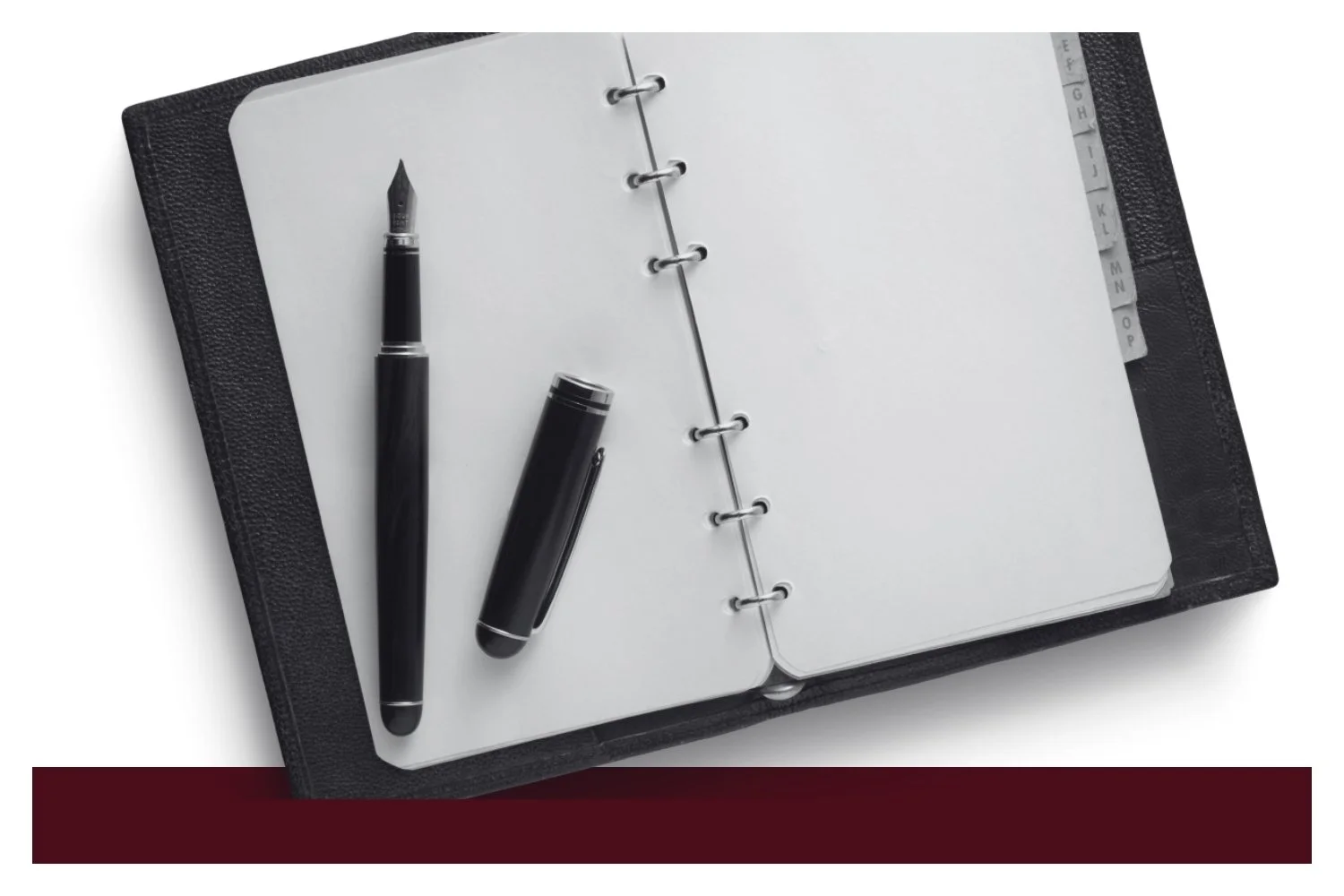 Open black notebook with metal ring binding, a fountain pen and a capped pen resting on the left page, and a vertical ruler along the right page margin.