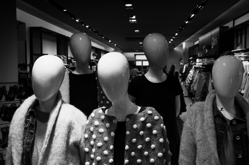 A group of mannequins in a clothing store display. They are wearing various garments, including sweaters and jackets, and are arranged in a staggered formation.