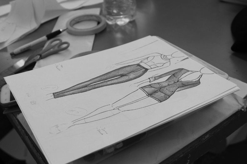 A fashion design sketch showing two outfits: a pair of slim-fit trousers and a tailored jacket with trousers.