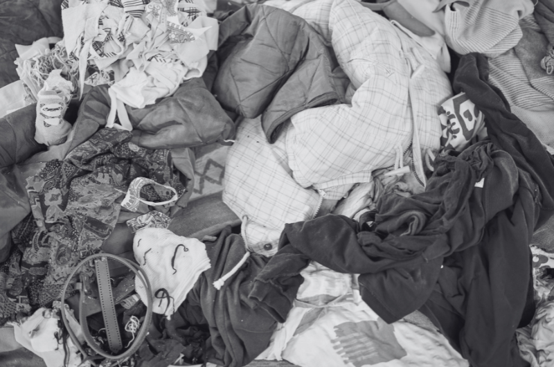 A pile of crumpled clothing with various patterns and textures, including plaid, floral, and solid dark fabrics.