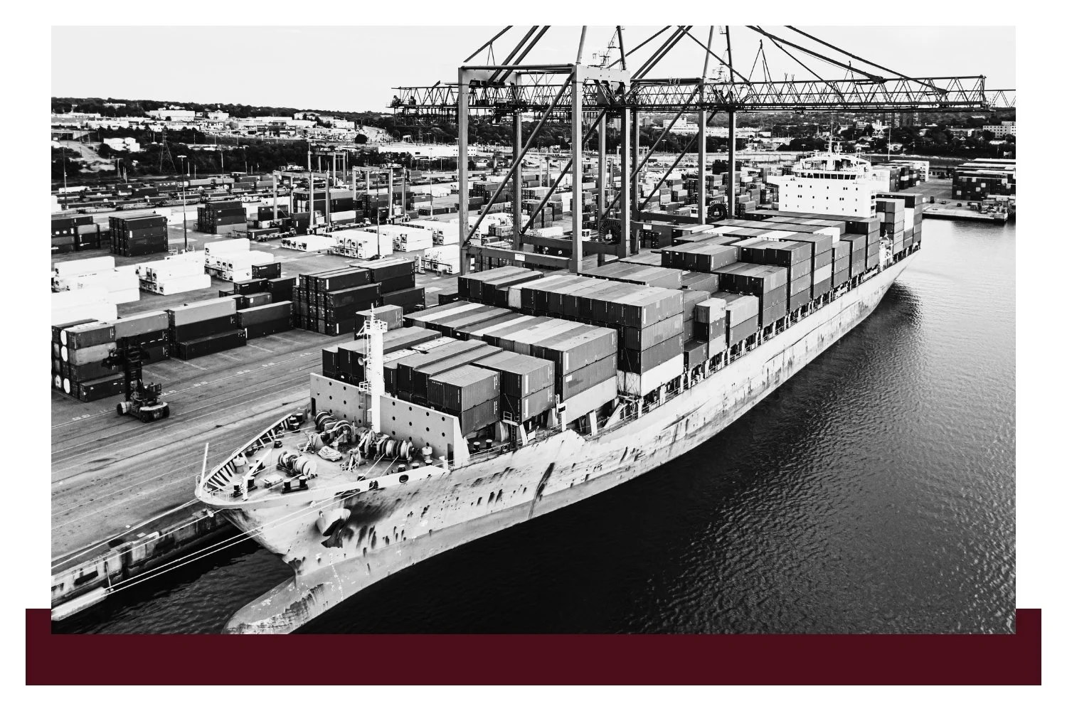 Aerial view of a large cargo ship docked along a river, loaded with rows of shipping containers and cranes above the deck.