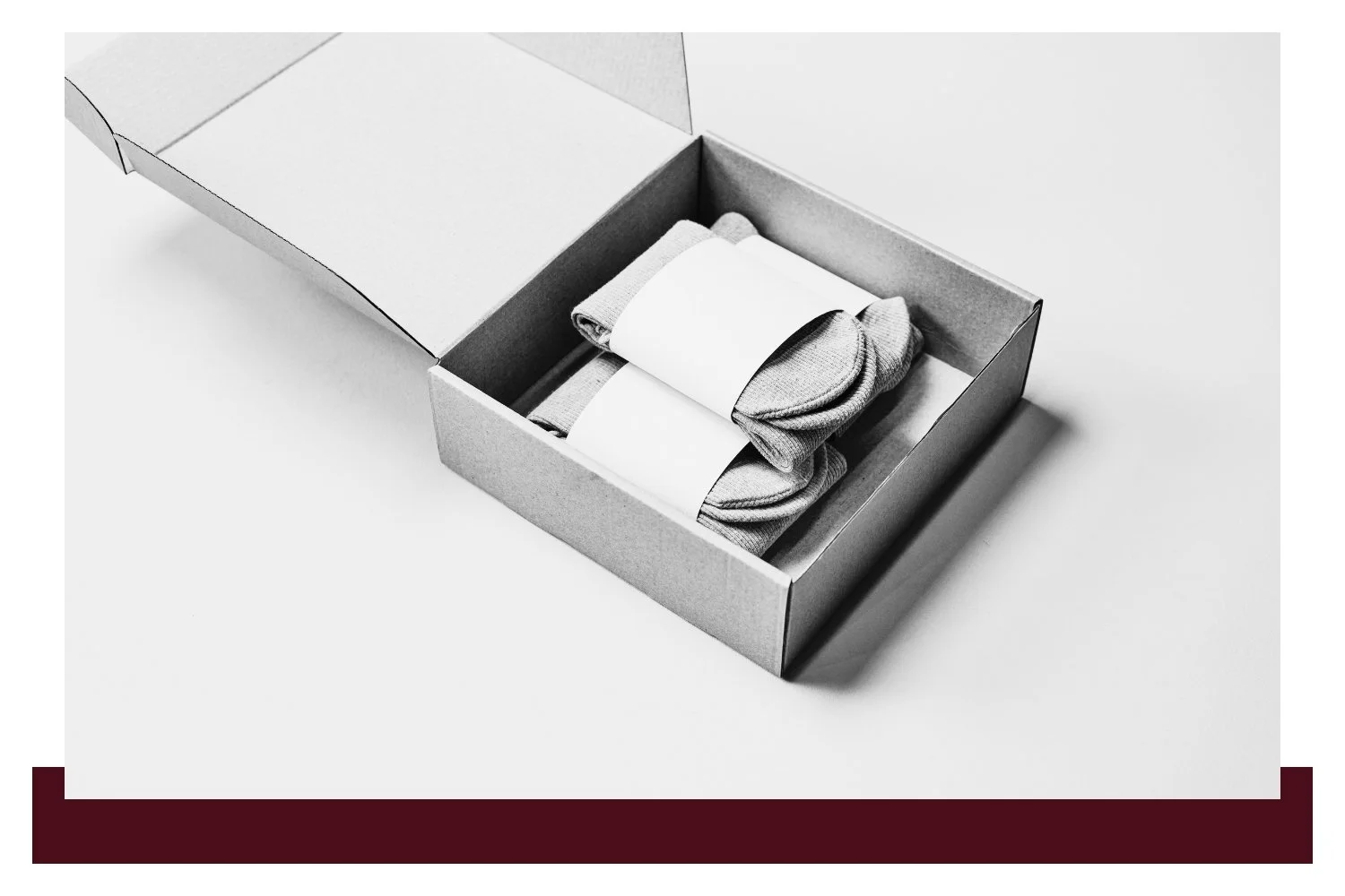An open gray cardboard box with folded tissue paper lining and several neatly stacked white paper sheets, photographed from above at an angle.