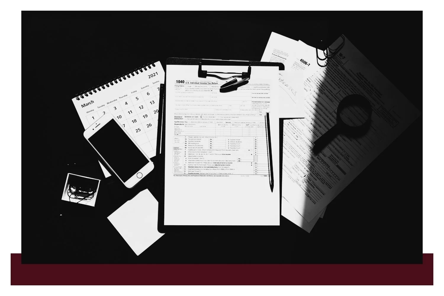 Scattered white papers and documents on a dark background, including a central sheet with printed tables and a chart, surrounded by partially visible forms and diagrams.