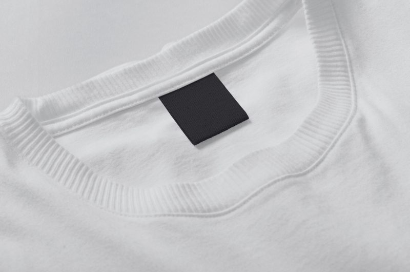 A close-up of a white t-shirt collar with a small black square tag sewn onto it.