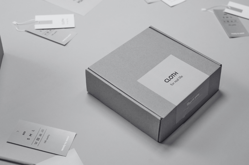 A gray cardboard box with a label that says "CLOTH" is on a gray surface. Several tags and cards are scattered around the box.