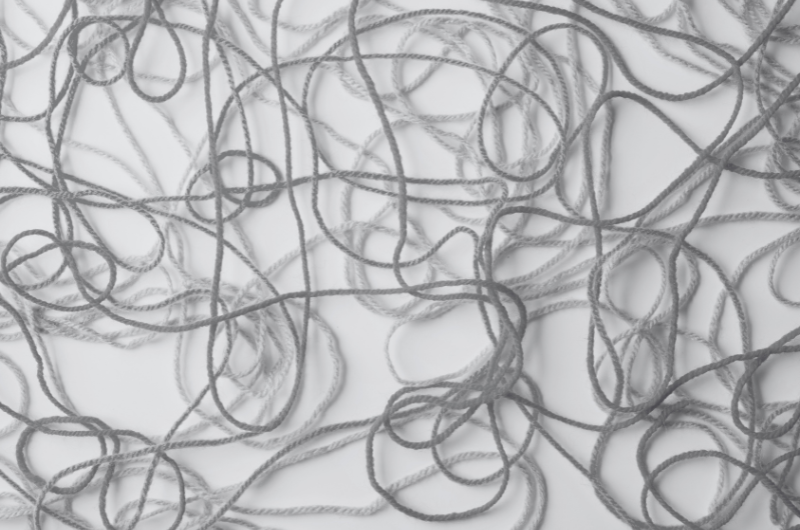 A tangled mess of light and dark grey yarn is spread across a white background.