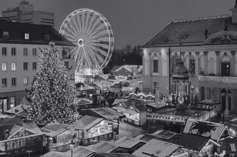 A festive Christmas market at night with a large, illuminated Christmas tree, a Ferris wheel, and numerous stalls below.