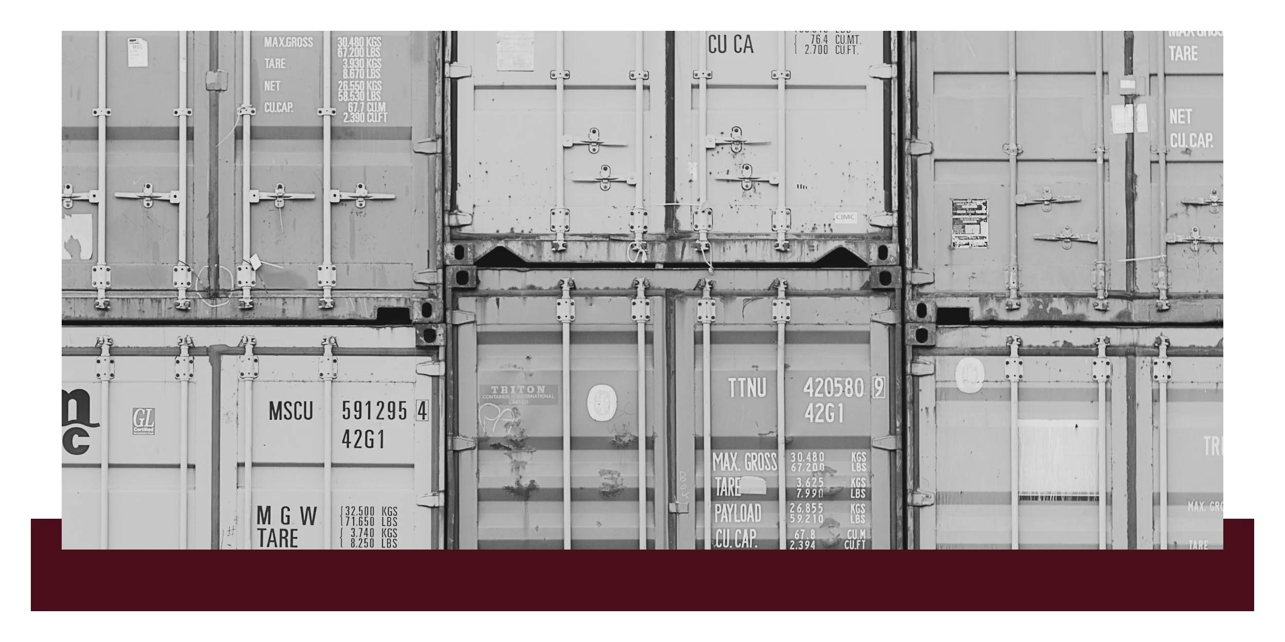 Black-and-white view of stacked shipping containers with visible stenciled codes and markings, shot from street level showing the doors and metal framework in an industrial yard.
