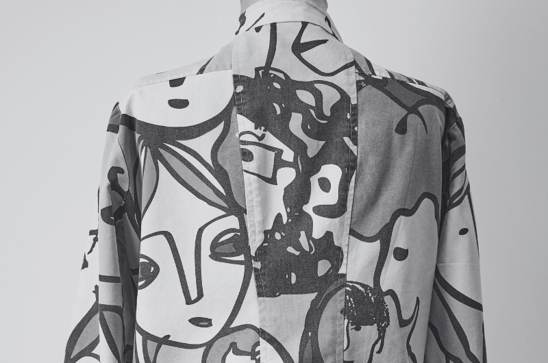 A black and white image of the back of a garment with a bold, abstract face pattern.