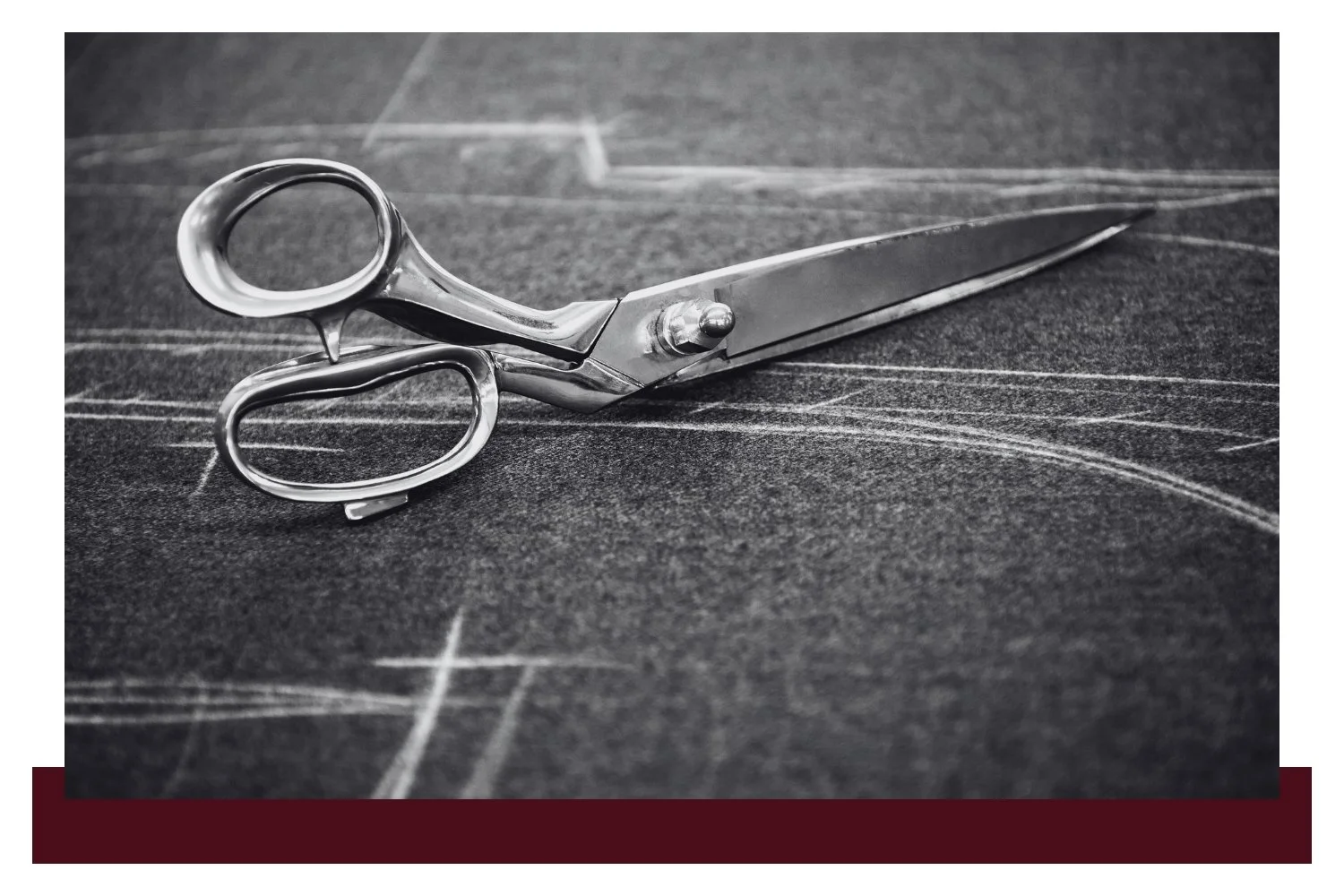 Closed metal scissors with silver blades and finger loops rest on a dark chalkboard with faint white grid lines and curved arcs.