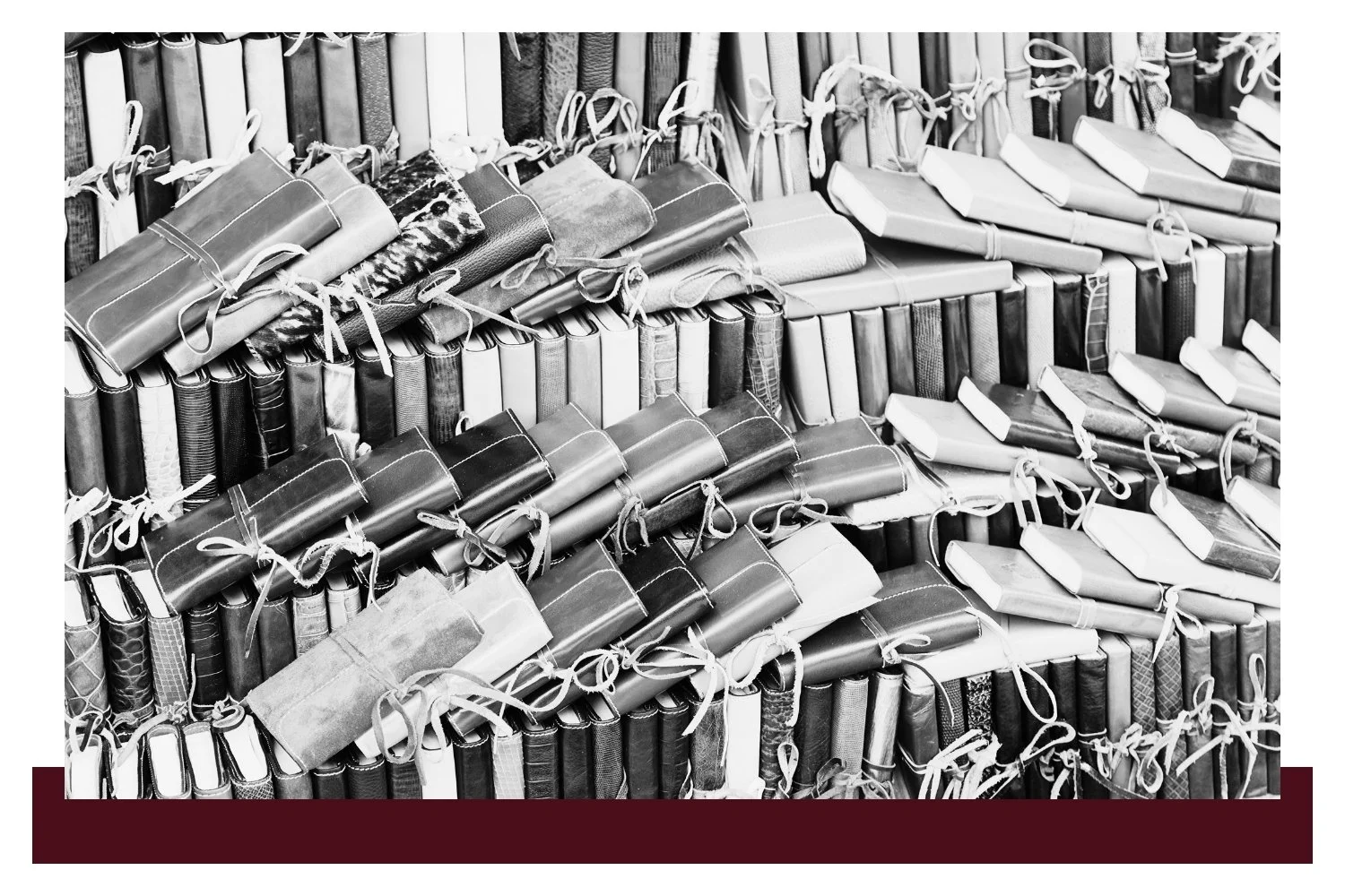 Black-and-white view of many stacked hardcover books with pages and spines tightly arranged on shelves, some tied with rope, creating repeating rows and columns.