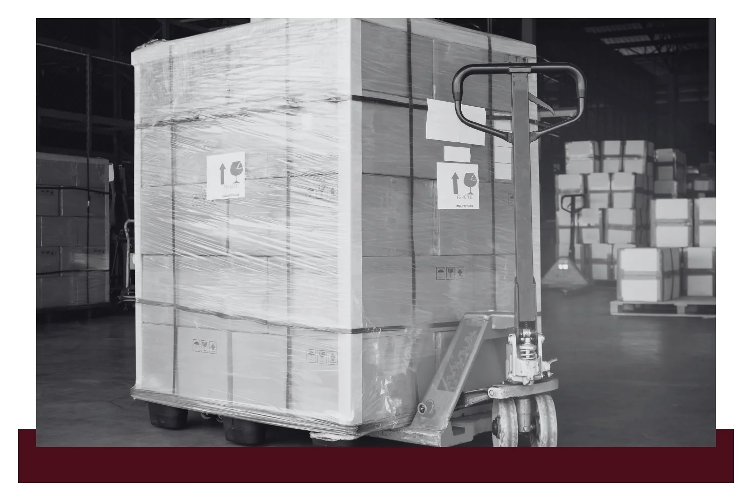 Black-and-white warehouse scene with large shrink-wrapped crates on pallets, each marked with a label, secured to a forklift at the foreground while more stacked boxes fill the background.