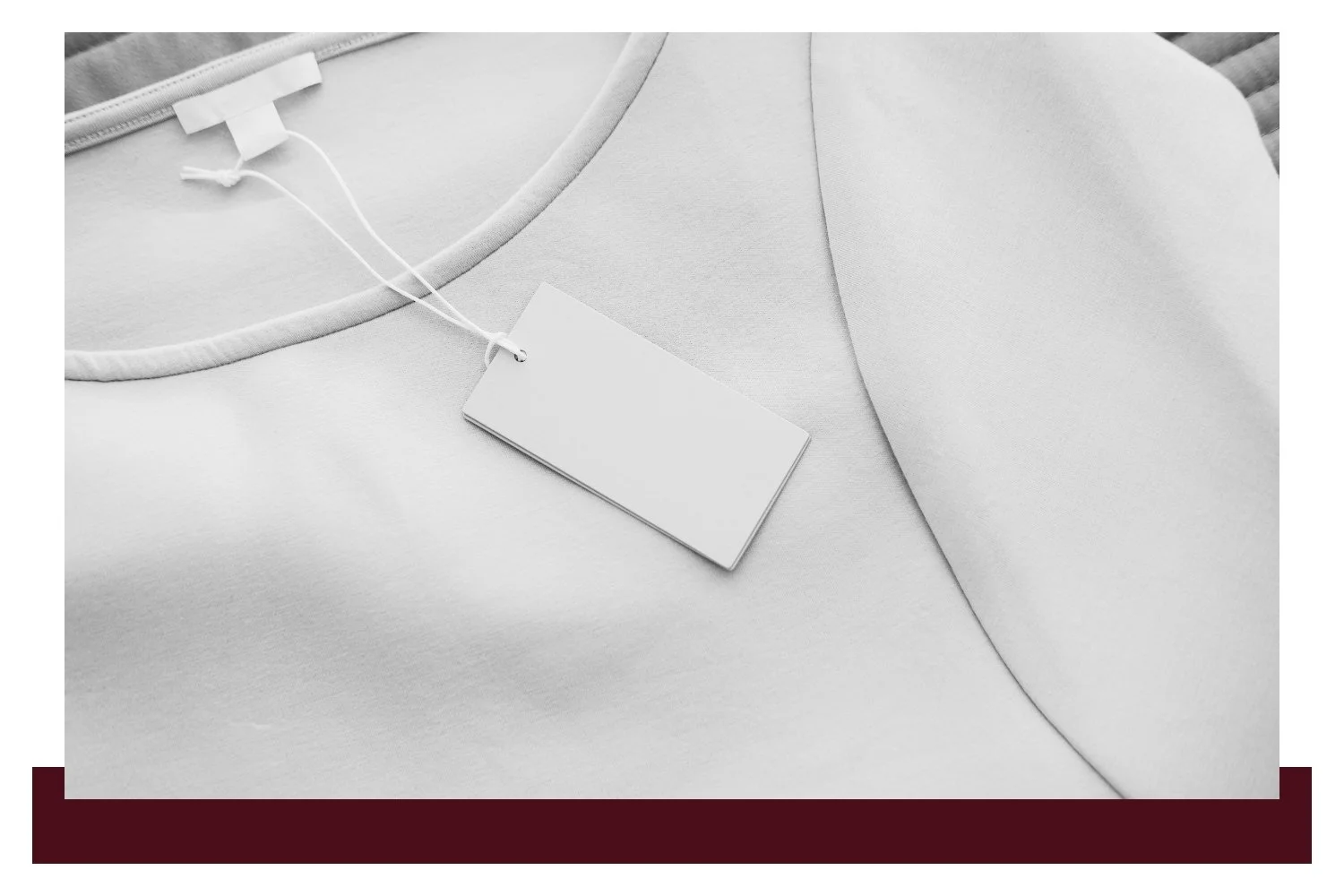 Close-up of a white garment with a dangling white fabric tag on a thin string, set against a softly lit background, with another tag partially visible.