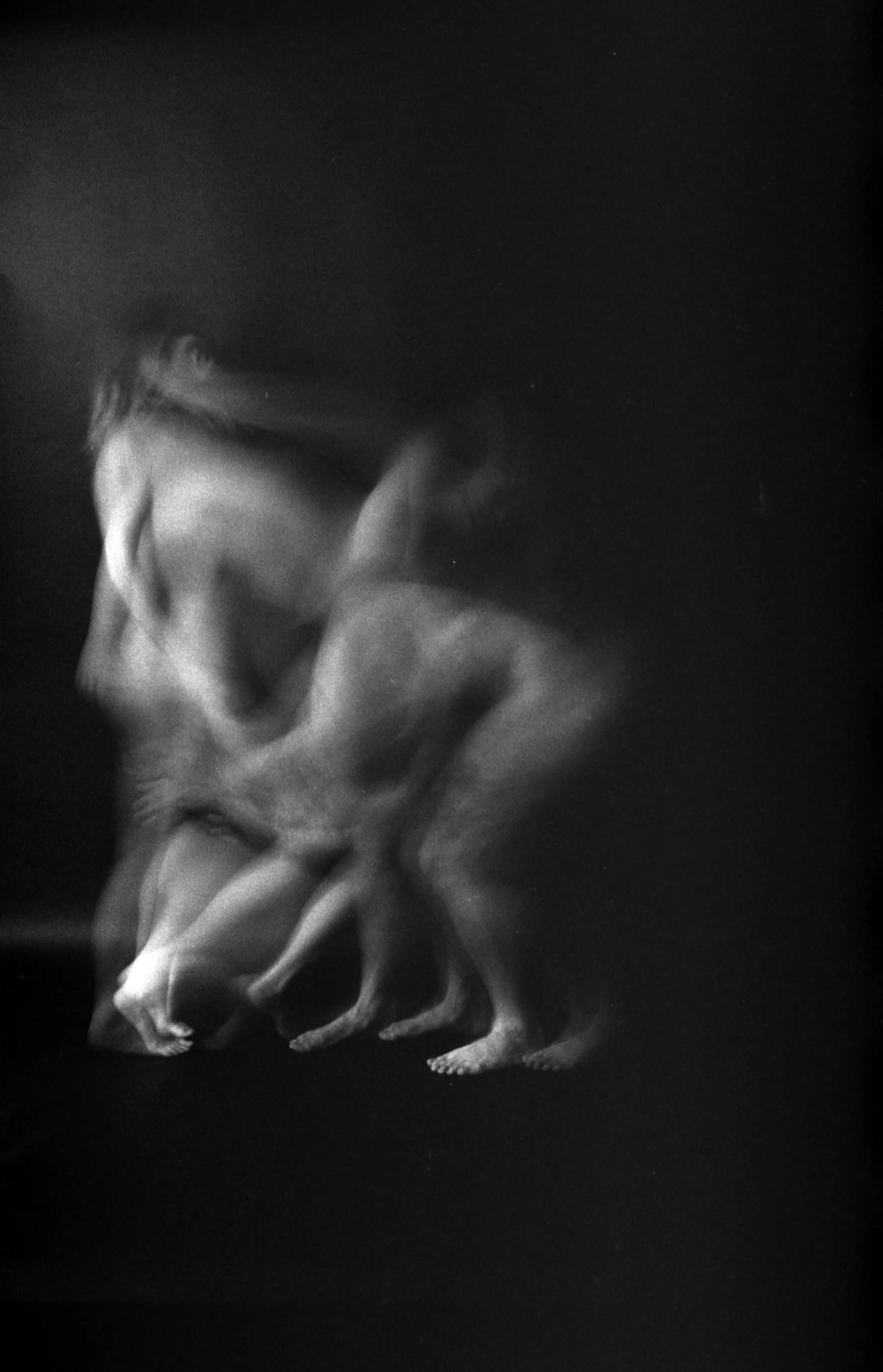 Black and white photo of a person with long hair covering their face, holding their head with their hands, with a dark background.