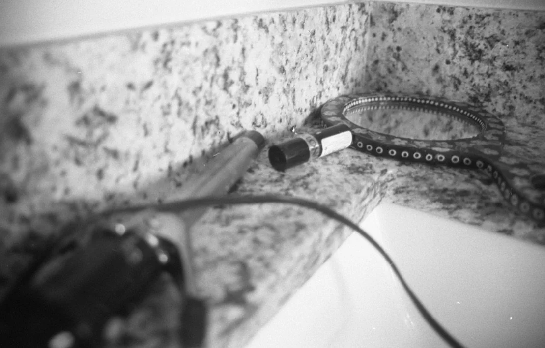 A close-up black and white photo of a snake curled on a granite countertop, with electrical cords and a flashlight nearby.